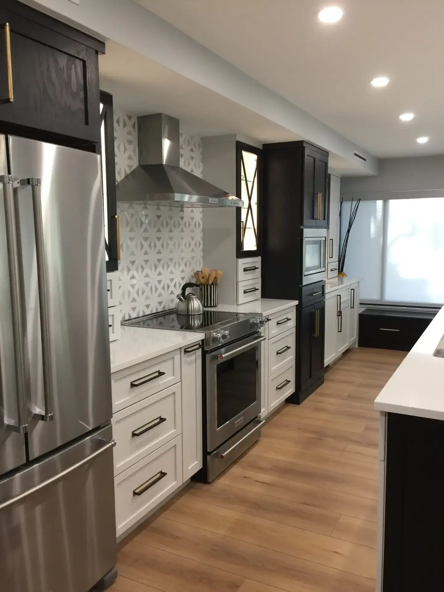 Two-tone kitchen with white shaker lower cabinets, dark espresso tall cabinets, brass pulls, quartz counters, and stainless appliances