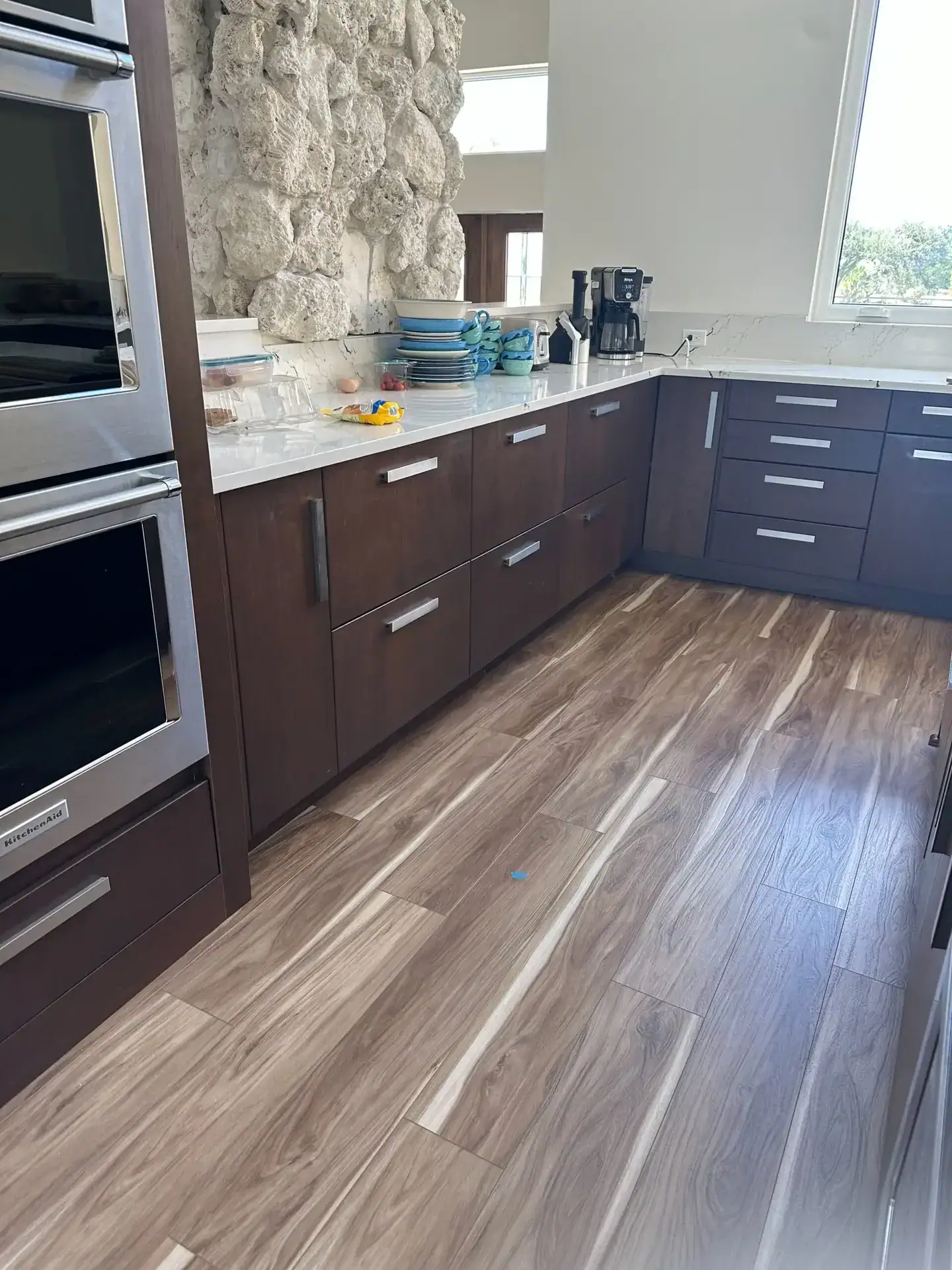Dark walnut flat-panel kitchen cabinets with stainless bar pulls, white quartz countertop and wood-look vinyl flooring