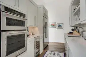 Light gray flat-panel kitchen cabinets with stainless steel double ovens, built-in fridge, wine cooler, and quartz countertops